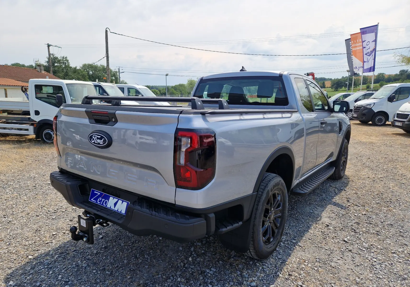 Ford Ranger Super Cabine gris Iconic vu en 3/4 arrière droit, avec marchepied, barres de plateau et attelage visible.