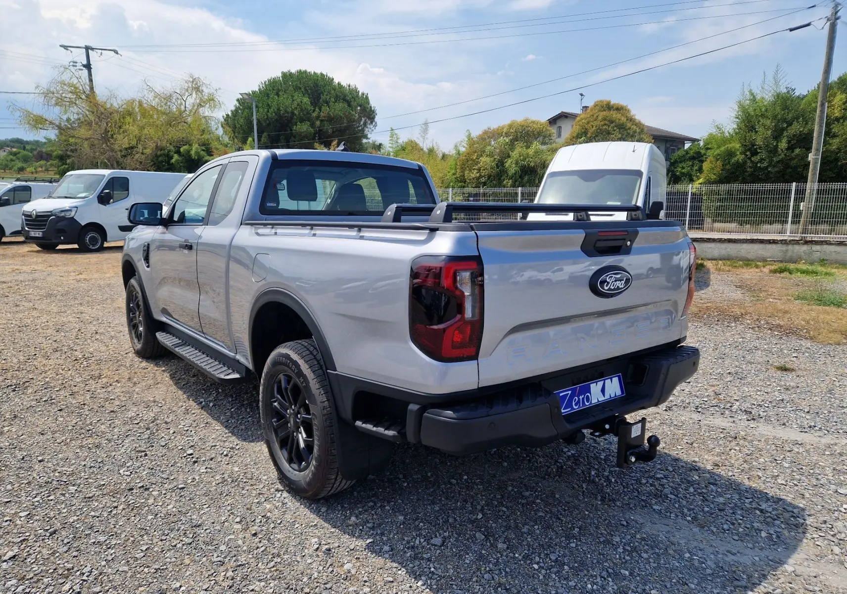 Ford Ranger Super Cabine gris Iconic vu en 3/4 arrière droit, avec barres de plateau et marchepied noir.
