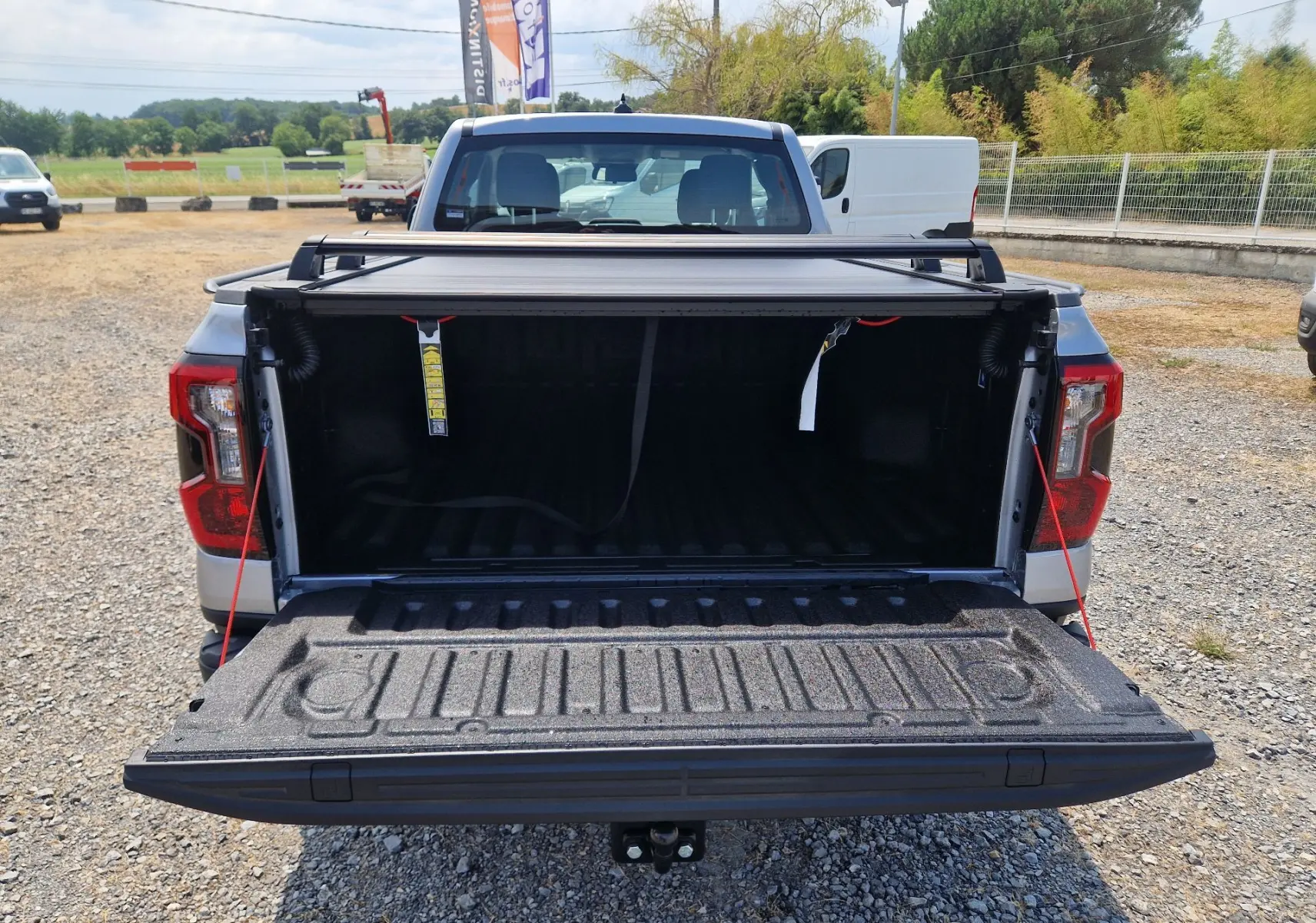 Vue arrière d’un Ford Ranger Super Cabine gris Iconic avec plateau ouvert et rideau rigide coulissant visible.