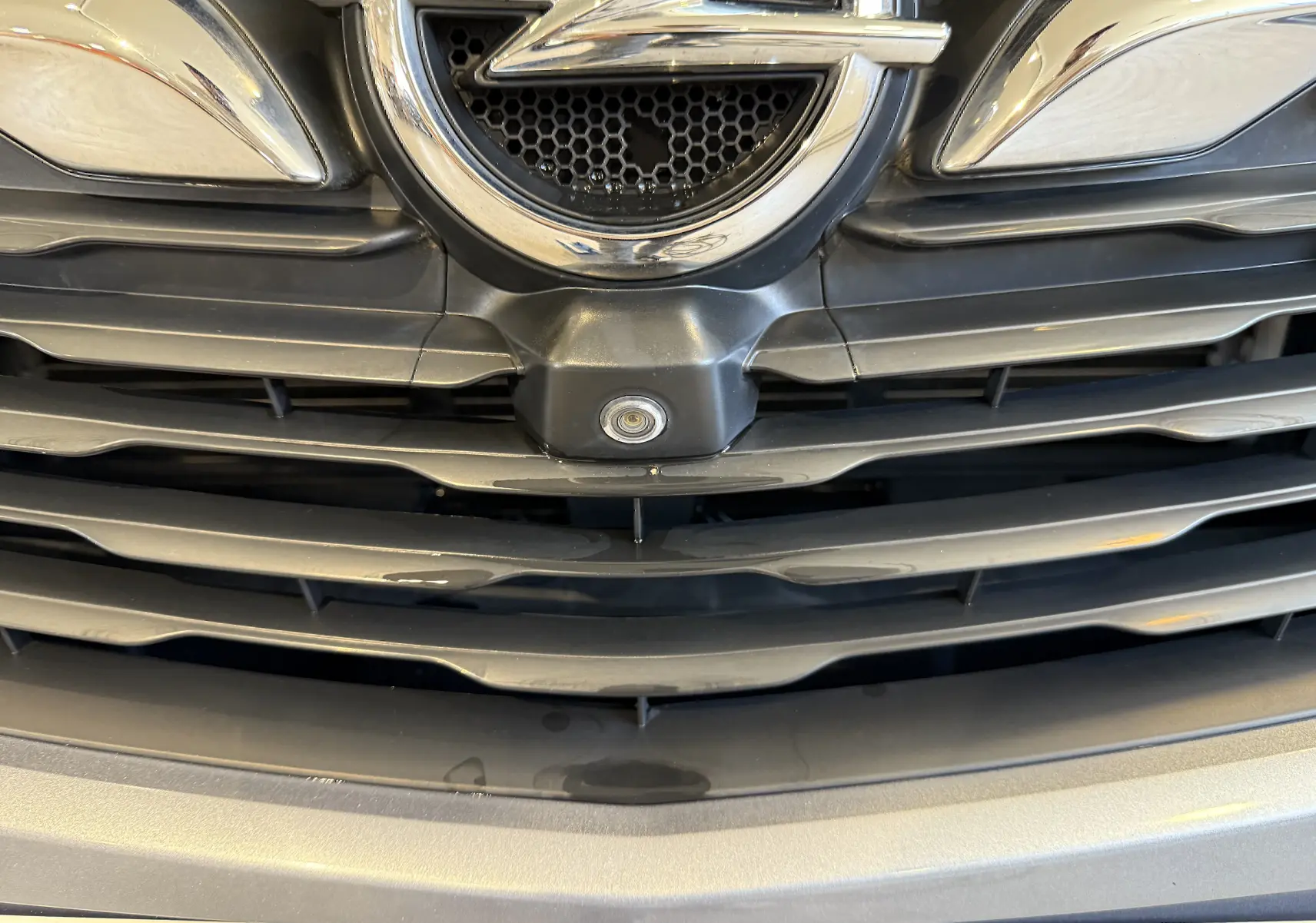 Gros plan sur la calandre gris Himalaya métal de l'Opel Grandland X avec logo et caméra avant intégrée.