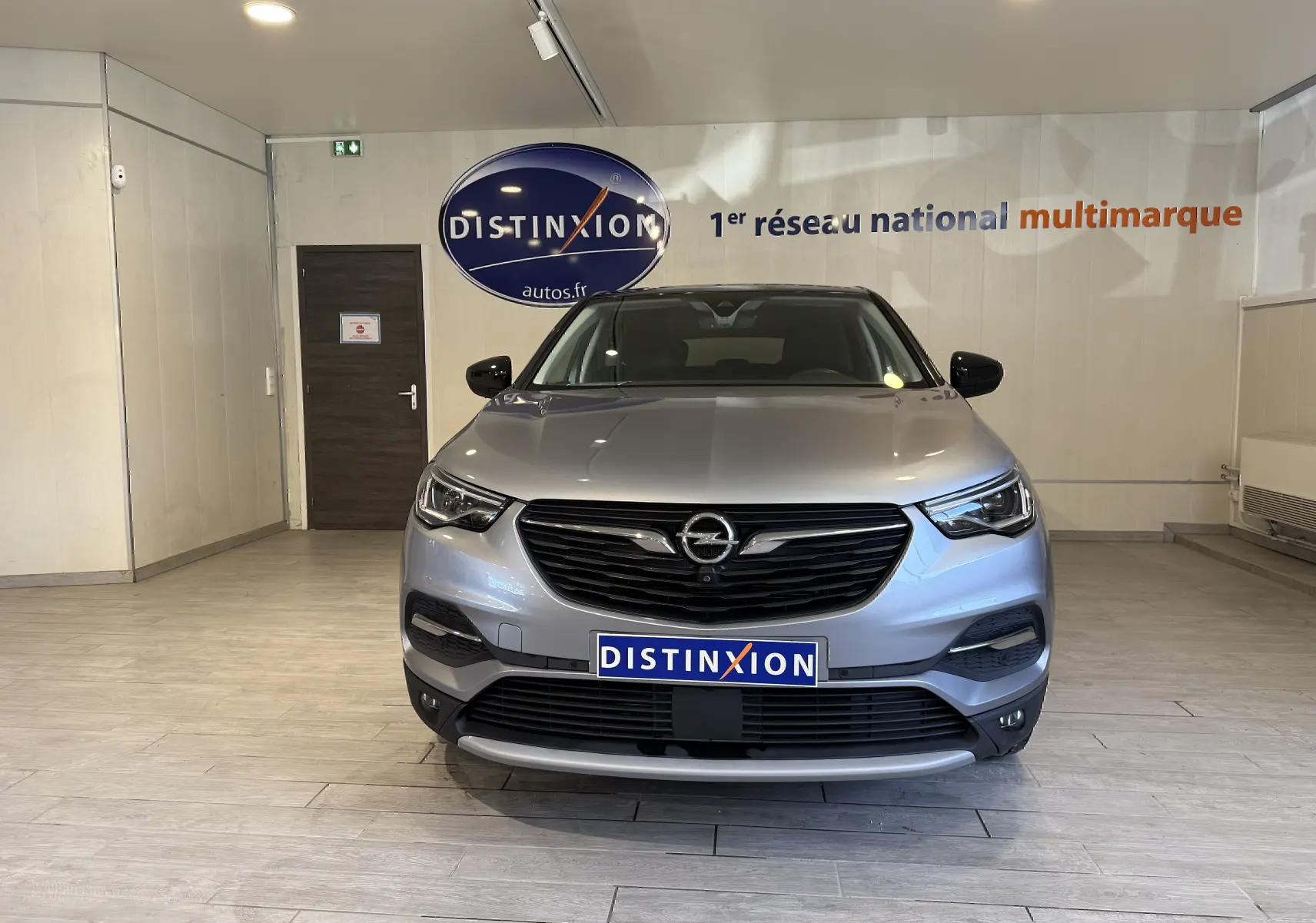 Vue frontale d'un Opel Grandland X gris Himalaya métallisé, avec calandre noire et logo Opel visible en showroom.