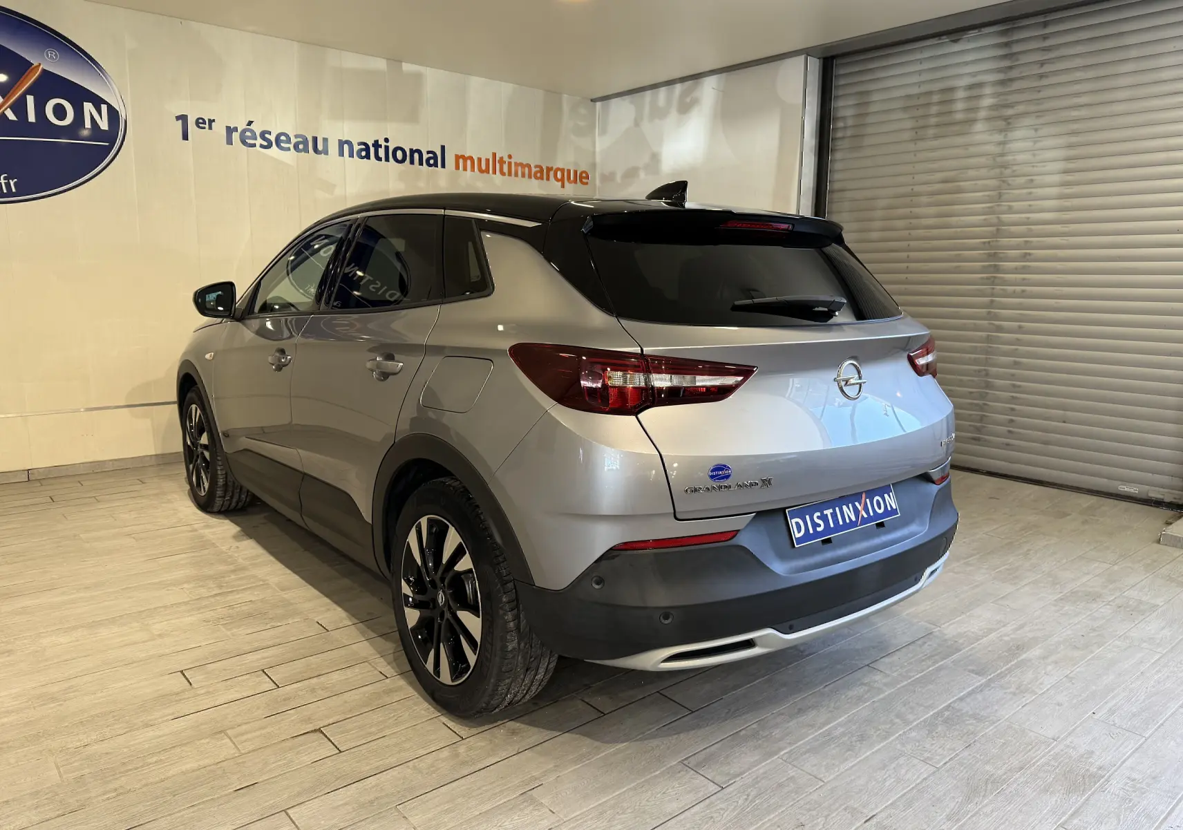 Vue 3/4 arrière droite d'un Opel Grandland X gris Himalaya métallisé avec toit noir et jantes noires en showroom.