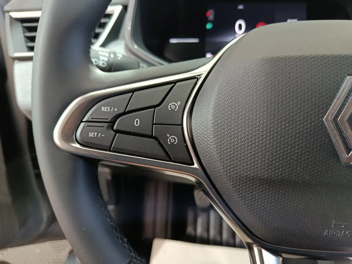 Gros plan sur le côté gauche du volant cuir synthétique de la Renault Clio gris clair, avec commandes multifonctions.