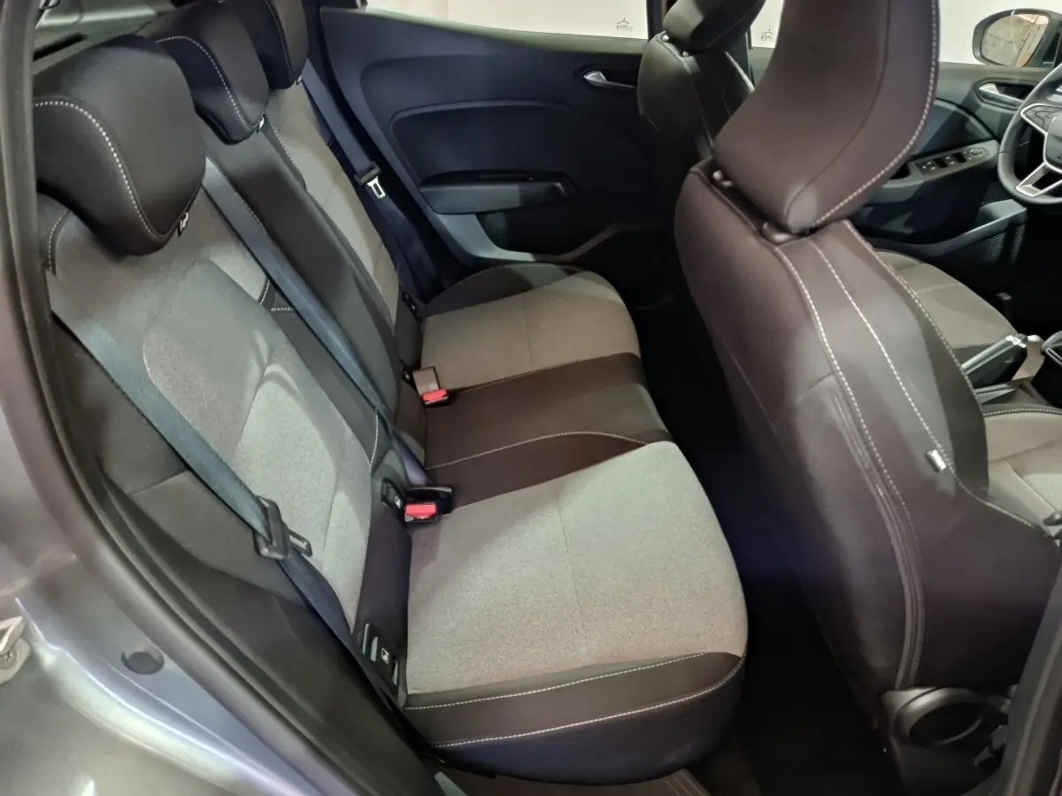 Vue intérieure côté arrière droit de la Renault Clio gris clair 2025, montrant la banquette tissu bicolore et les sièges avant.