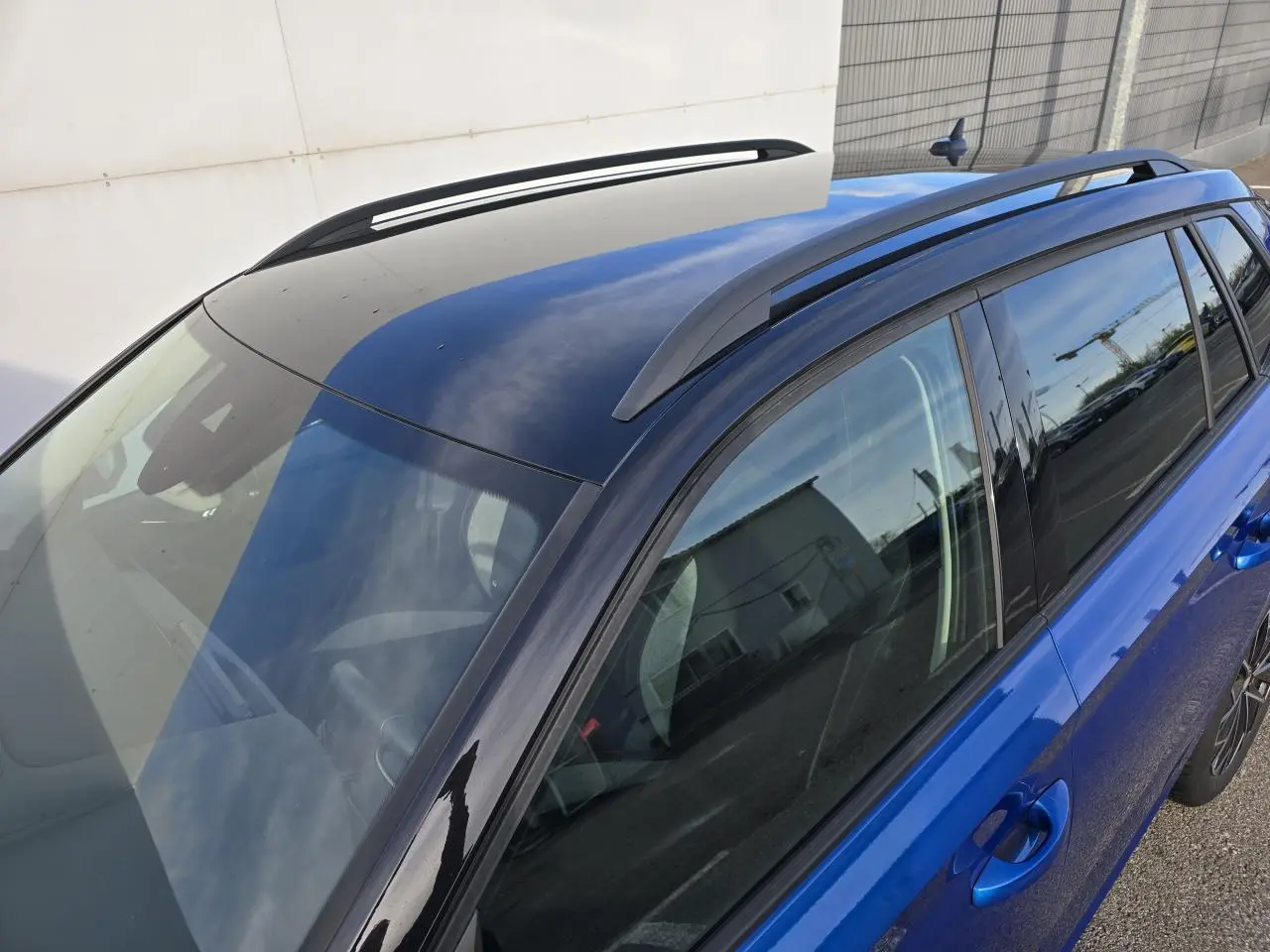 Vue plongeante côté droit du Skoda Kamiq 2025 bleu racing avec toit noir et barres de toit noires.