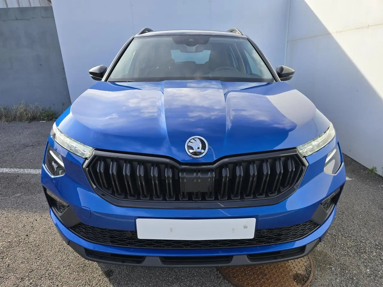 Vue frontale d'un Skoda Kamiq bleu racing avec calandre noire et toit noir visible en arrière-plan.