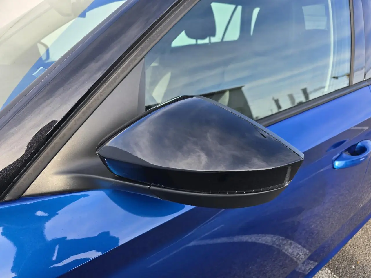 Gros plan sur le rétroviseur côté gauche noir brillant d’un Skoda Kamiq bleu racing avec toit noir.