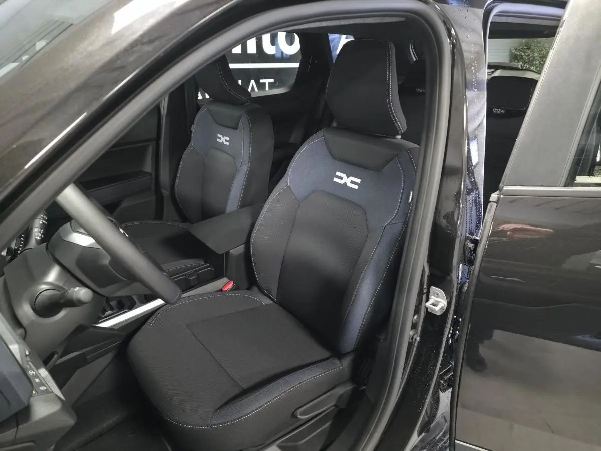 Vue intérieure côté conducteur du Dacia Duster 1.6 Hybrid 2025 noir nacré, sièges Denim bleu avec logo DC brodé.