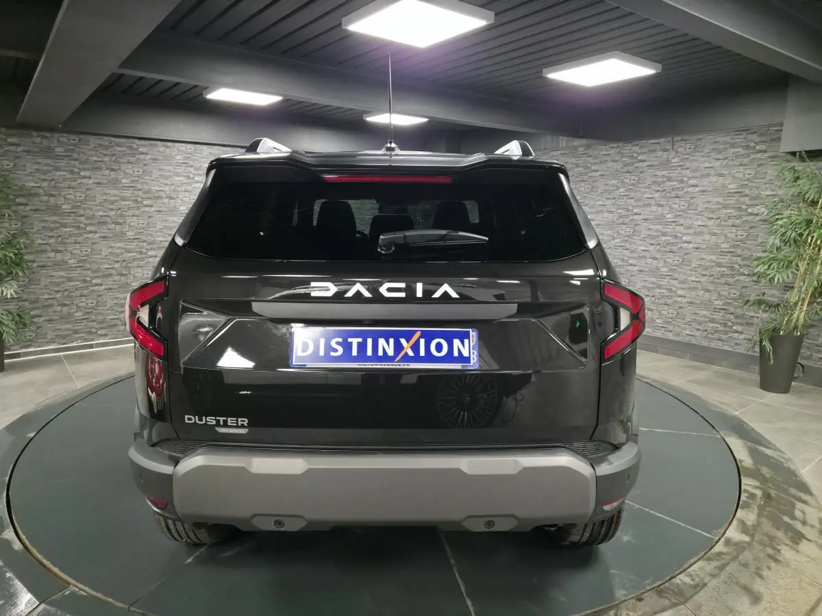 Vue arrière d'un Dacia Duster noir nacré 2025 avec logo DACIA inversé et plaque Distinxion.