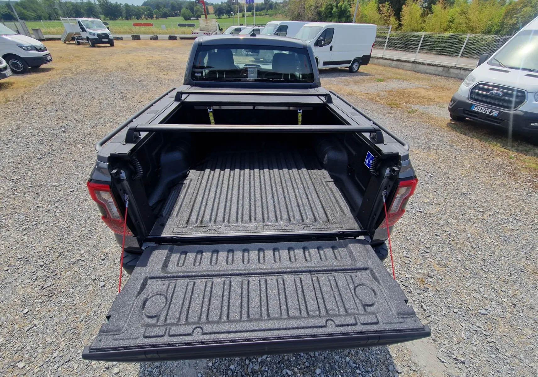 Vue arrière d'un Ford Ranger Super Cabine gris carbone avec plateau ouvert et rideau rigide coulissant visible.