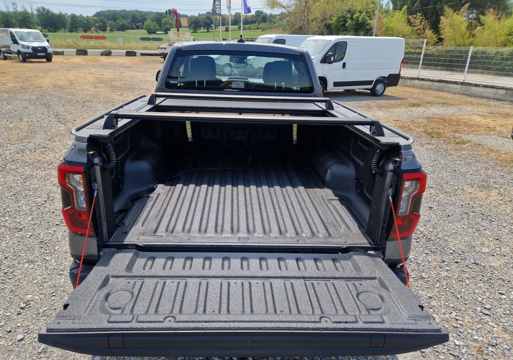 Vue arrière d'un Ford Ranger Super Cabine gris carbone avec plateau ouvert et rideau rigide coulissant visible.