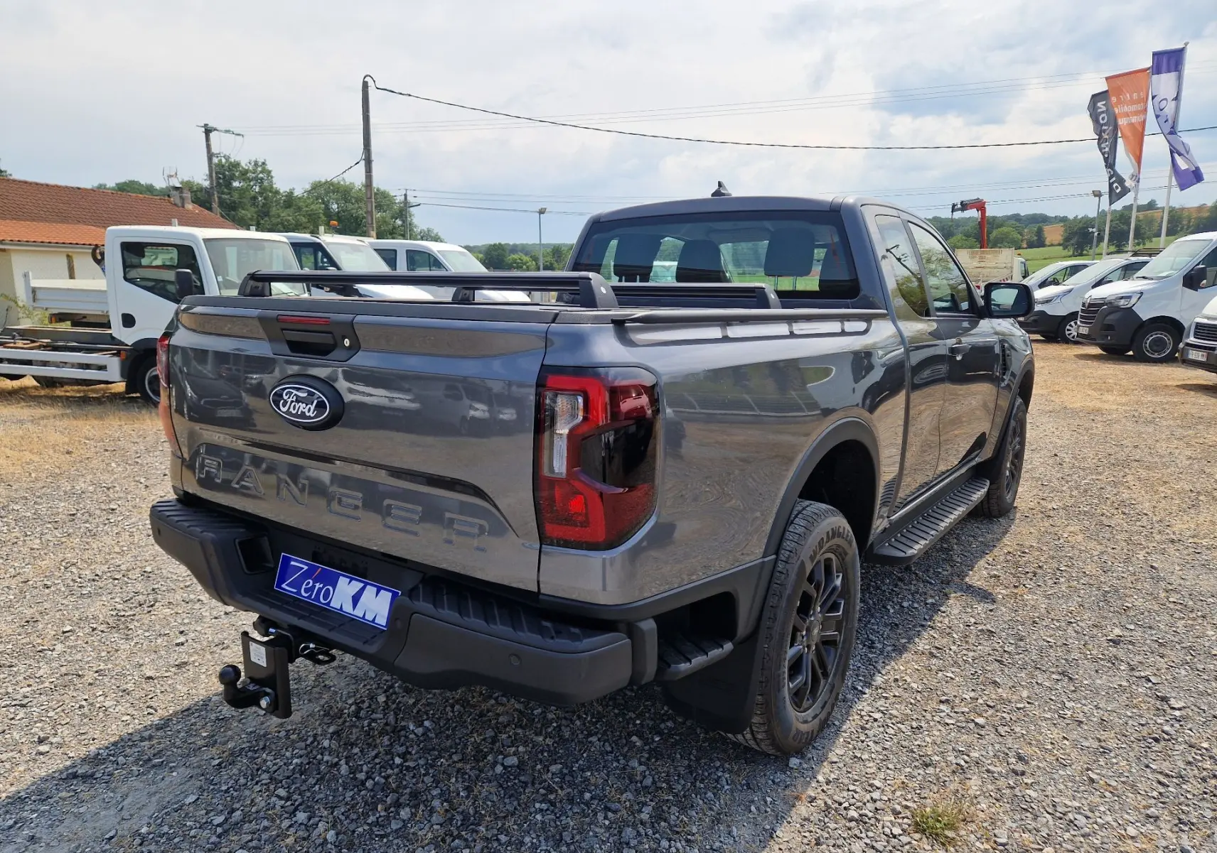Ford Ranger Super Cabine gris carbone vu en 3/4 arrière droit, avec rideau de plateau rigide et barres de toit.