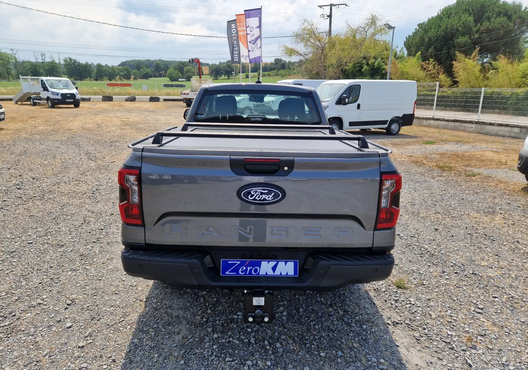 Vue arrière d’un Ford Ranger Super Cabine gris carbone avec rideau de plateau rigide et attelage visible.