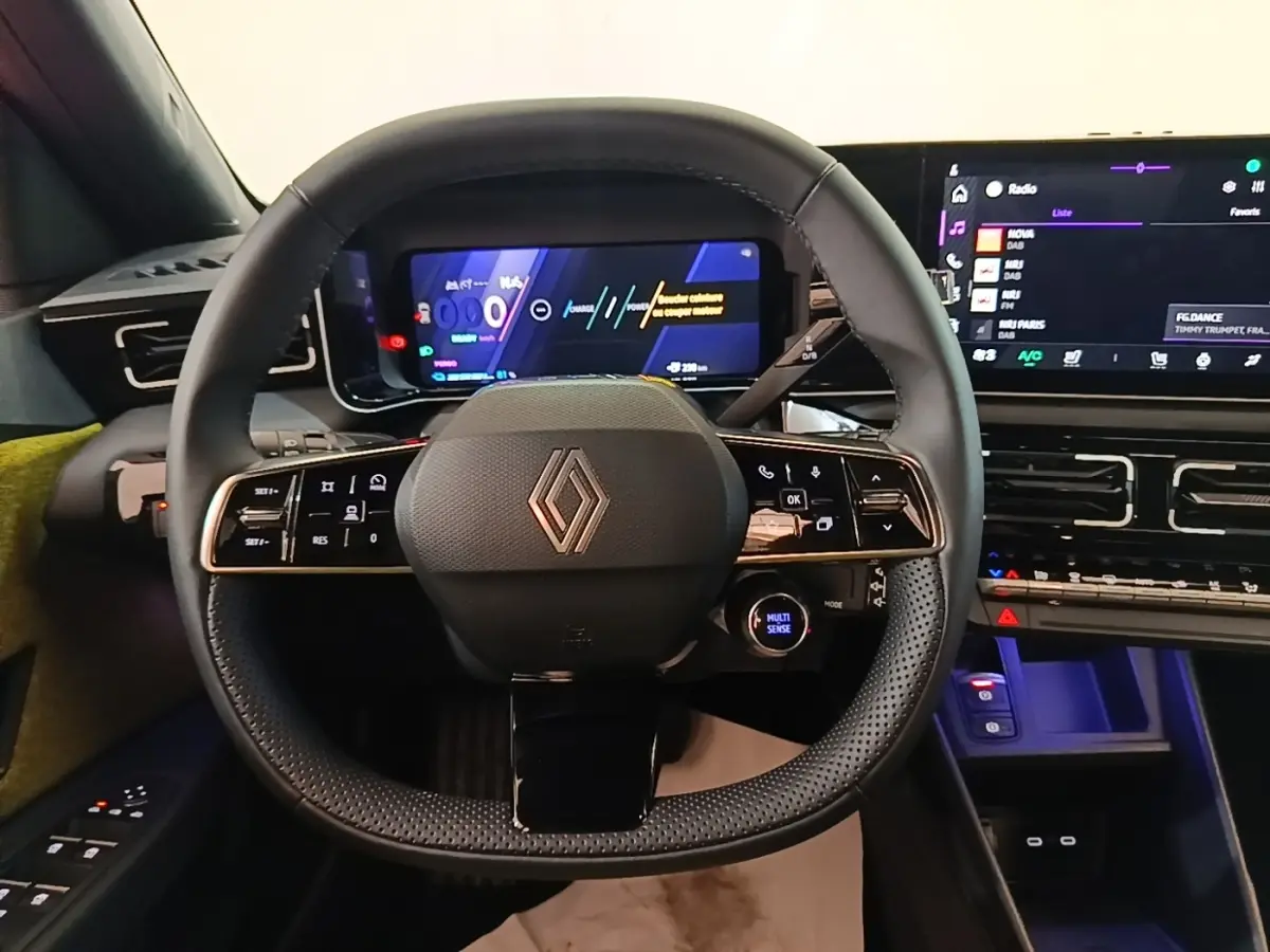 Vue frontale du volant noir perforé de la Renault R5 électrique 2024 avec tableau de bord numérique et écran tactile.