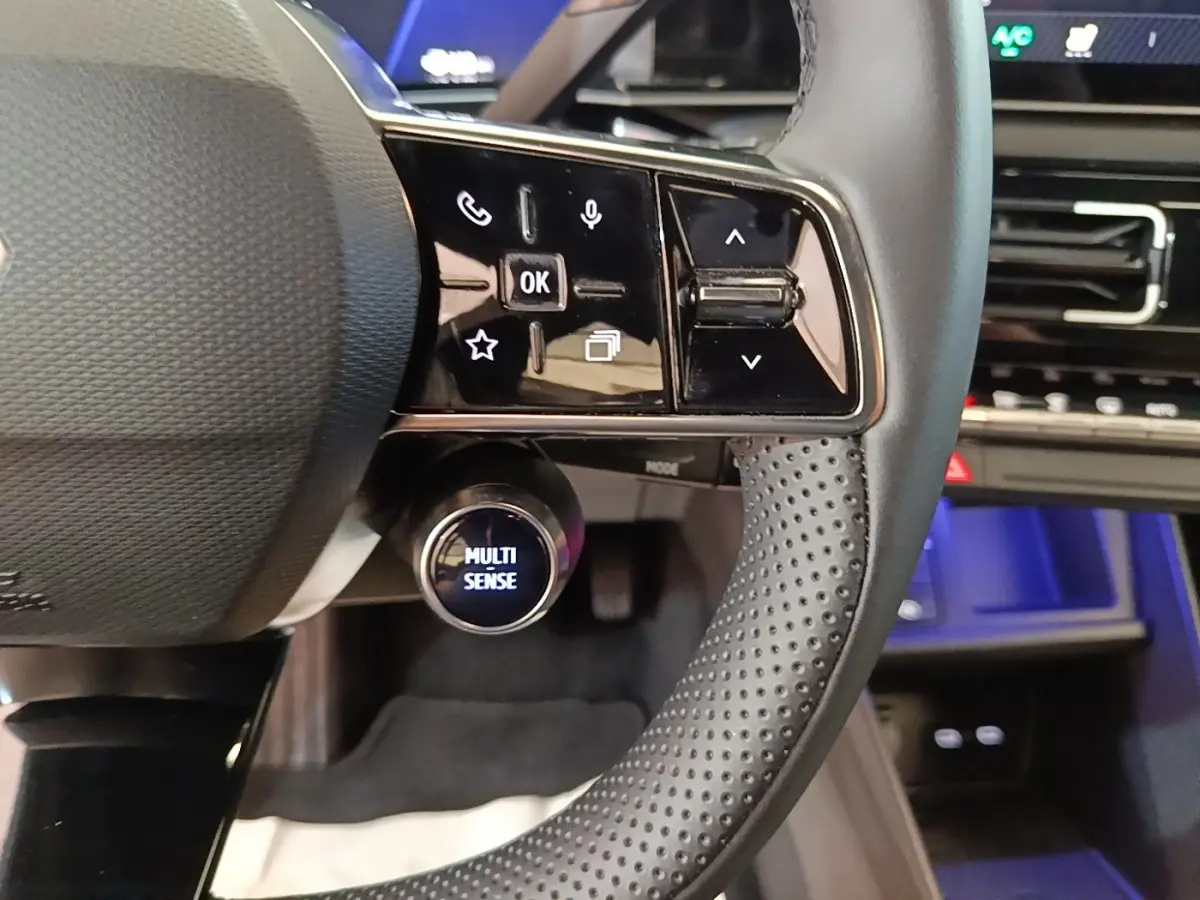 Gros plan sur le volant perforé et les commandes tactiles du Renault R5 électrique 2024, ambiance intérieure moderne.