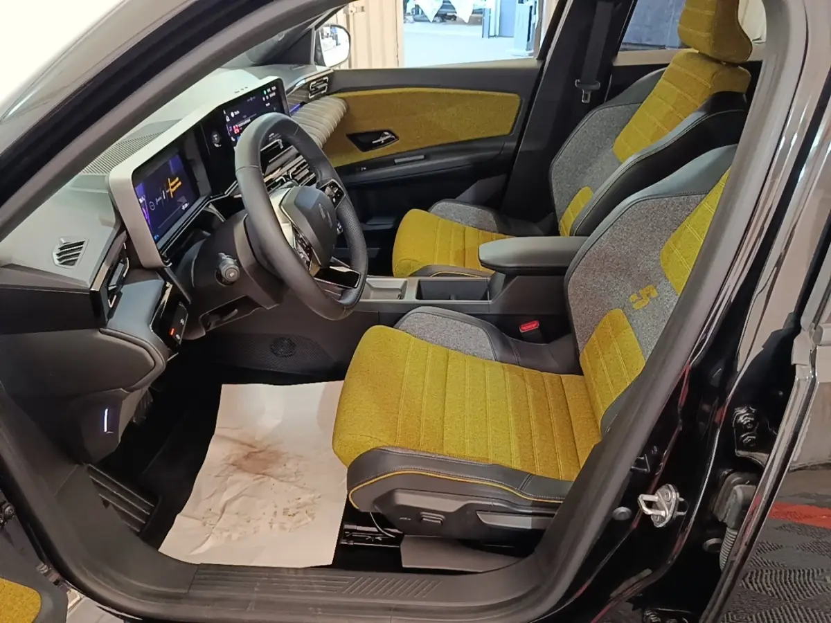 Vue intérieure côté conducteur de la Renault R5 Iconic 2024, sièges tissu jaune et gris avec tableau de bord numérique.