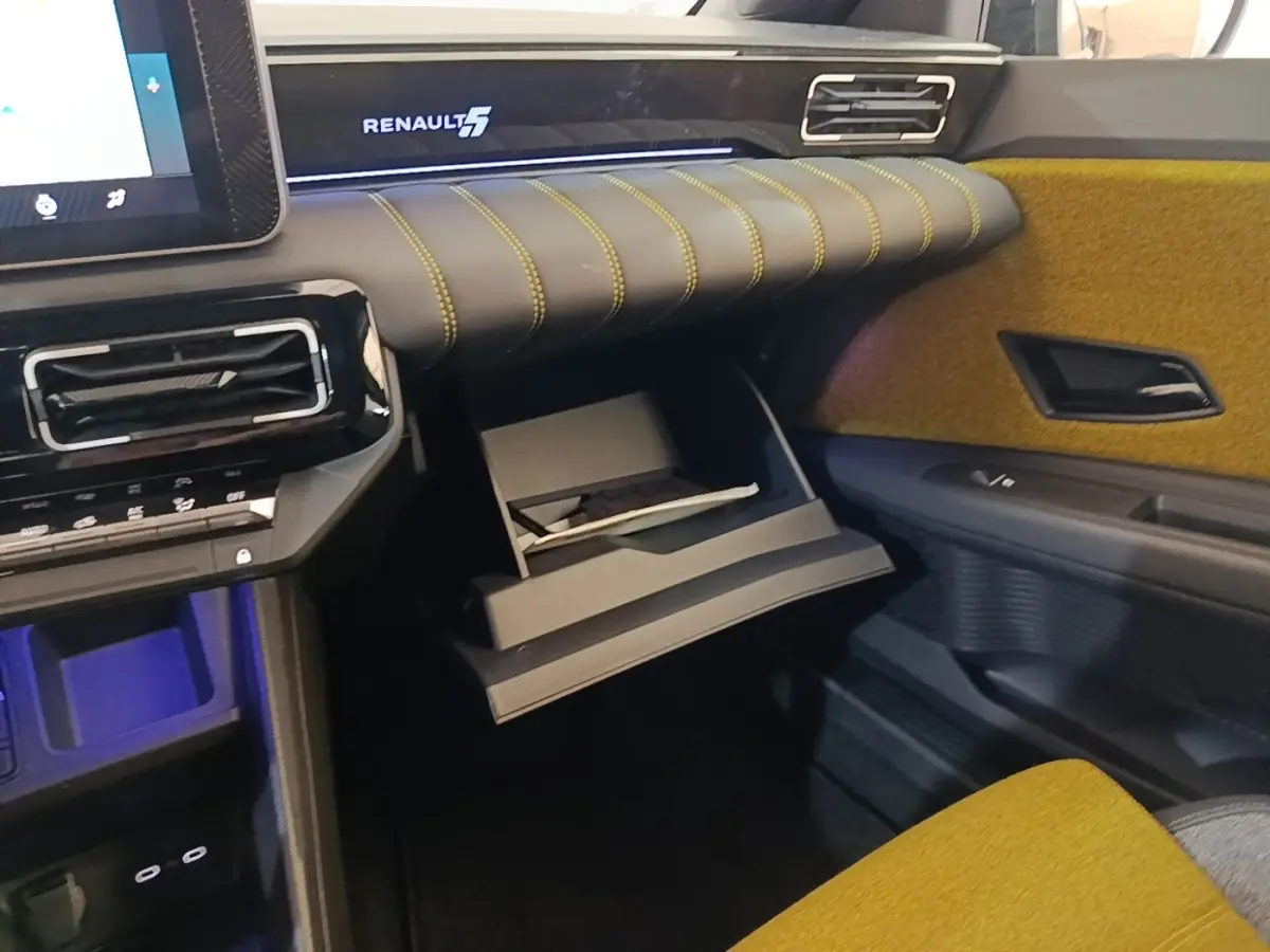 Intérieur Renault 5 Iconic 2024 côté passager, tableau de bord noir avec surpiqûres jaunes et boîte à gants ouverte.