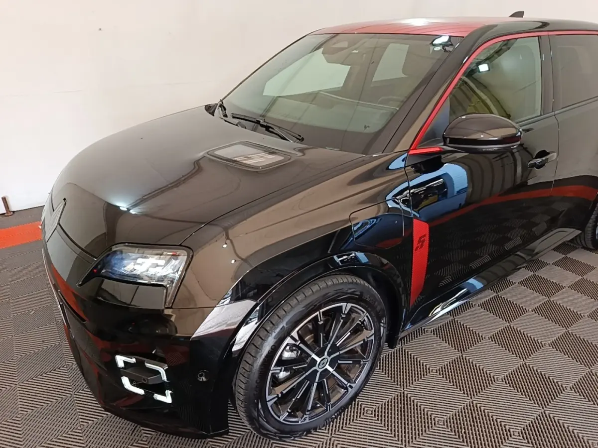 Vue 3/4 avant droite de la Renault R5 Iconic électrique noire avec toit et détails rouges, jantes noires distinctives.
