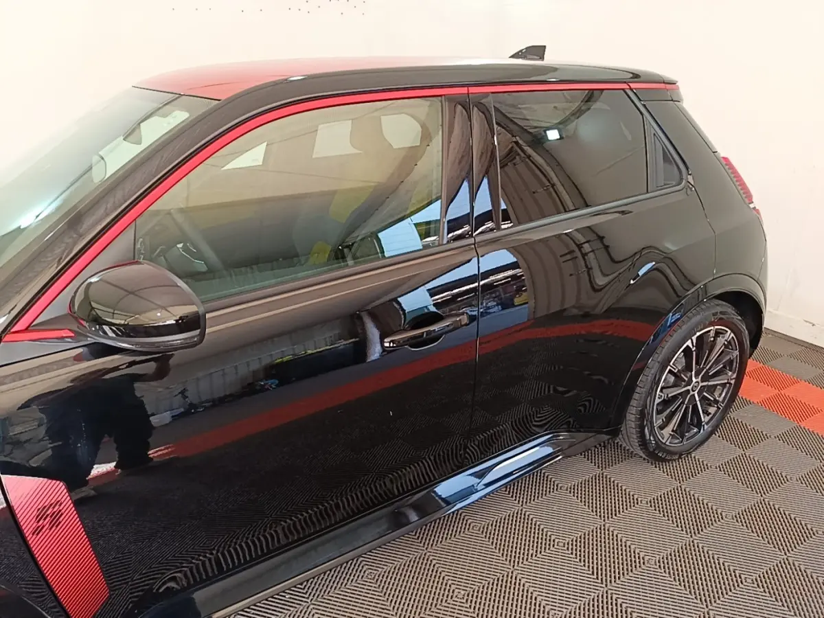 Vue latérale droite d'une Renault R5 électrique 2024 noire avec toit et détails rouges, jantes alliage noires.