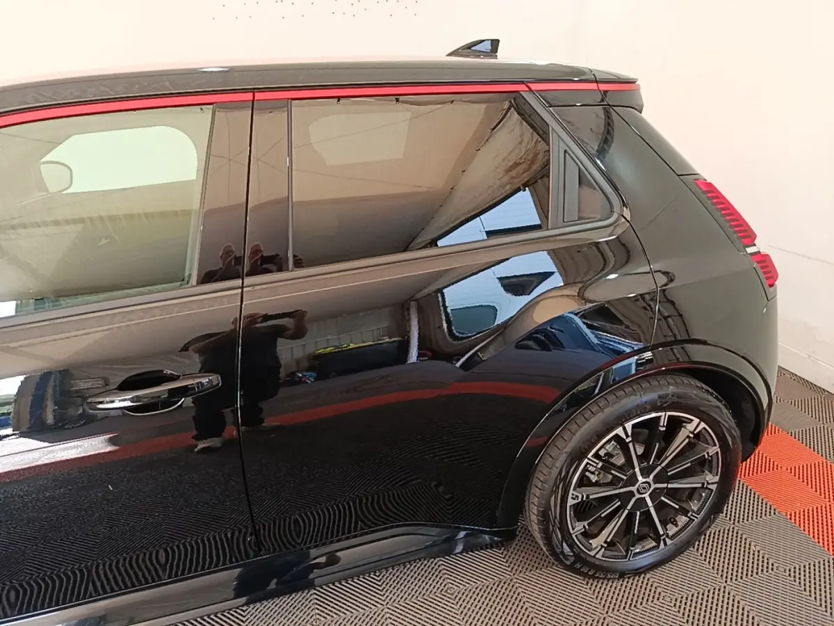 Vue latérale droite arrière d'une Renault R5 électrique 2024 noire avec jantes alliage et bande rouge décorative sur la vitre.