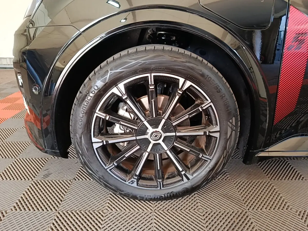 Gros plan sur la roue avant droite noire avec jante alliage bicolore et détail rouge sur la carrosserie.
