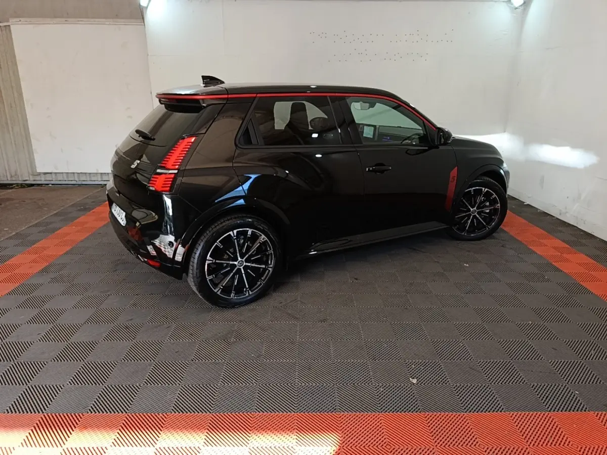 Vue 3/4 arrière droite de la Renault R5 Iconic électrique noire avec détails rouges et jantes noires en intérieur showroom.