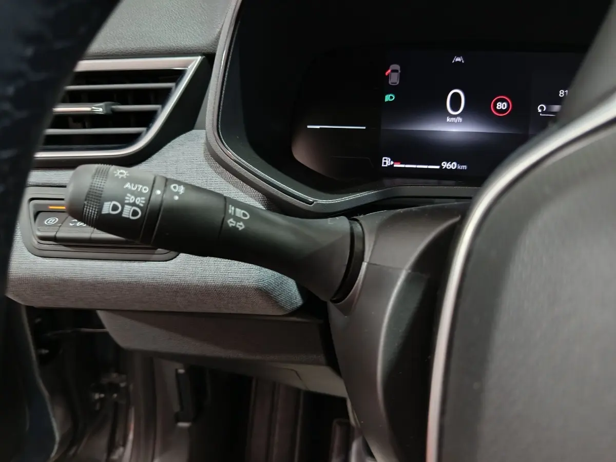 Gros plan intérieur sur la commande des phares et le combiné d'instruments numérique de la Renault Clio gris clair Evolution Blue dCi 100.