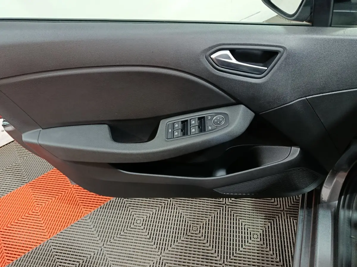 Vue rapprochée de la porte avant droite de la Renault Clio gris clair, avec commandes électriques des vitres et poignée intégrée.