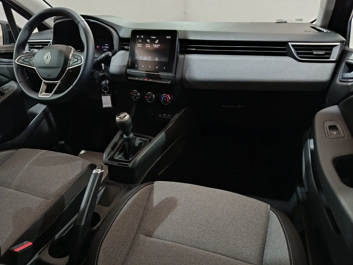 Vue intérieure avant de la Renault Clio Evolution Blue dCi 100 2025, tableau de bord gris clair avec écran tactile central et volant multifonctions.