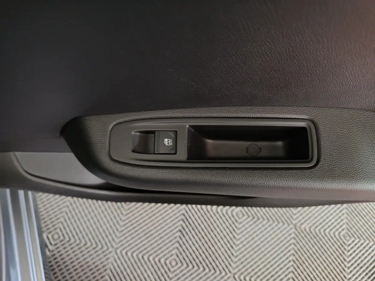 Gros plan sur la commande de lève-vitre côté porte intérieure d’une Renault Clio gris clair.