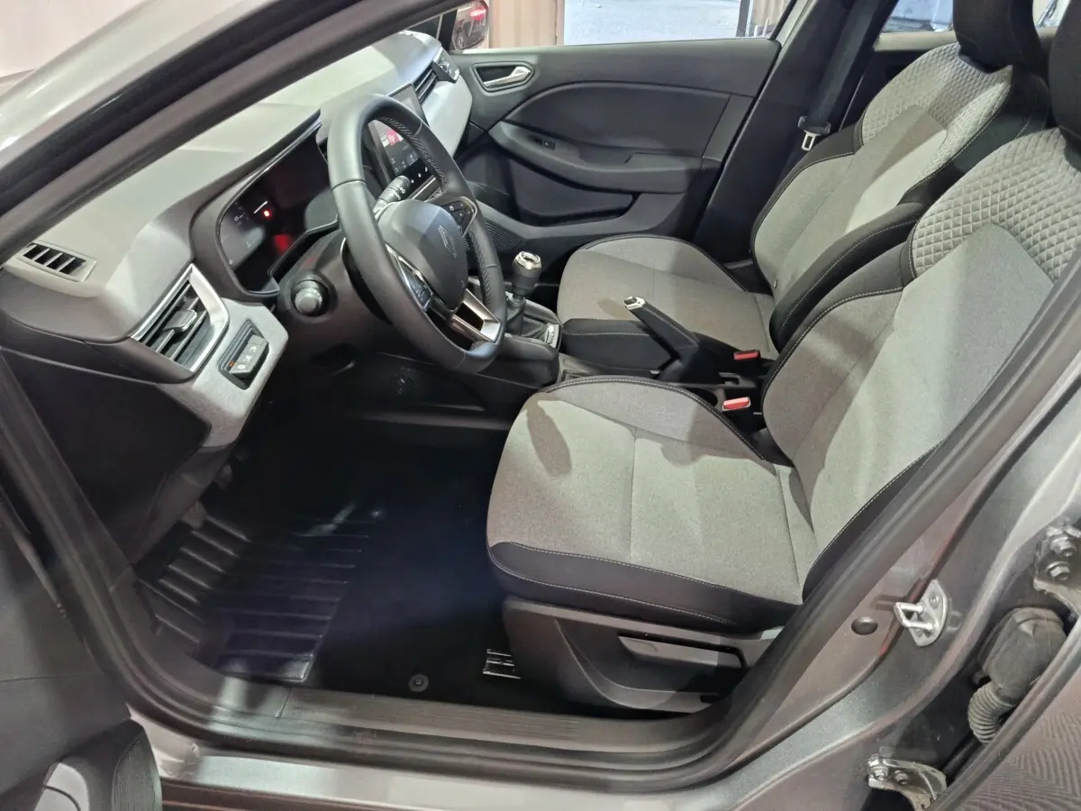 Vue intérieure côté conducteur de la Renault Clio gris clair 2025, volant multifonctions en cuir synthétique et sièges tissu gris.