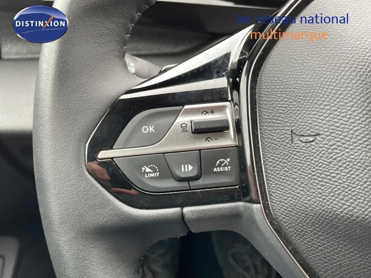 Gros plan sur les commandes à gauche du volant noir du Peugeot 408 1.2 Hybrid 2025, avec boutons multifonctions visibles.
