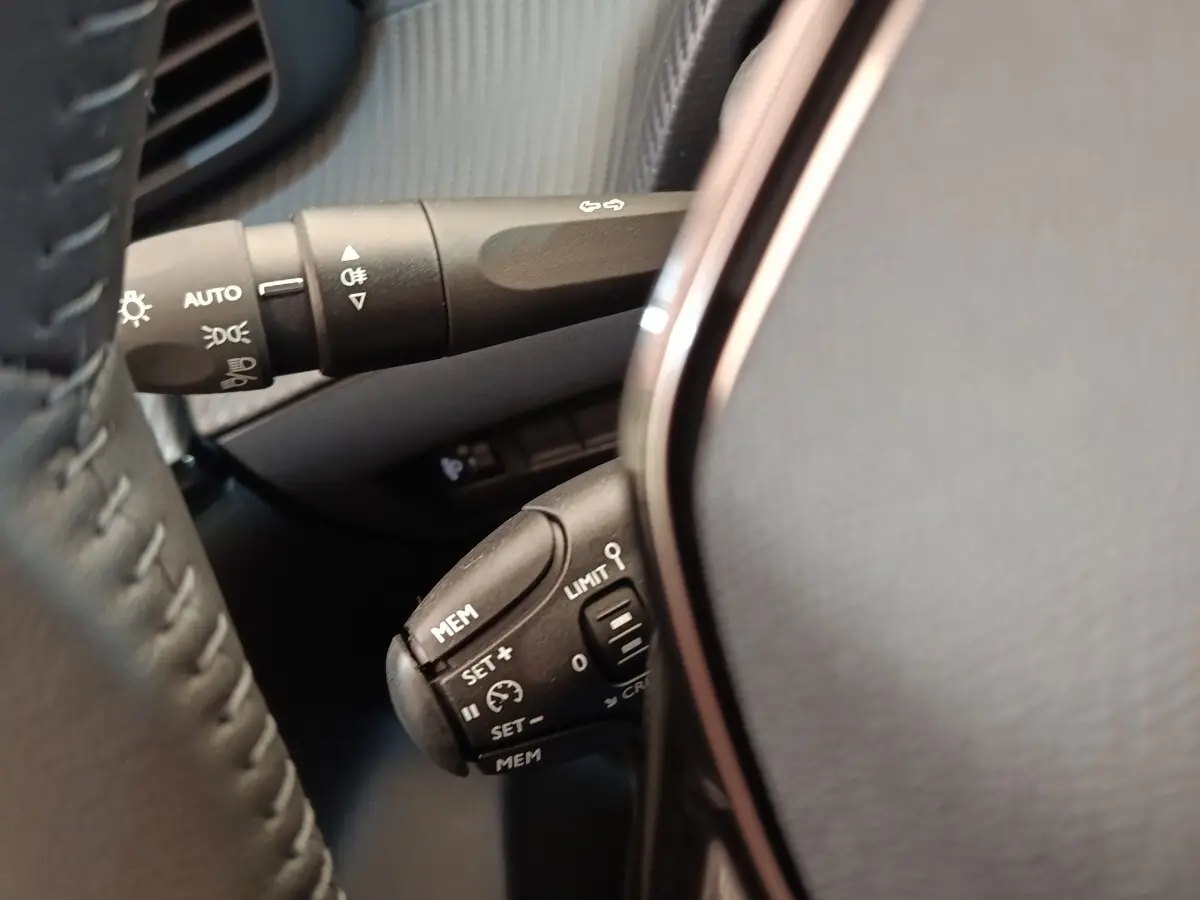 Gros plan sur la commande multifonction du régulateur de vitesse au volant cuir noir du Peugeot 208 électrique blanc.