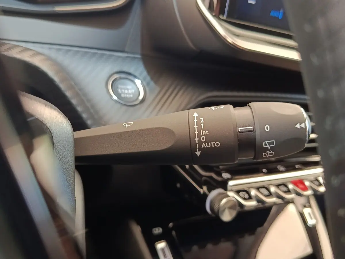 Gros plan sur la commande d’essuie-glace et le bouton démarrage dans l’habitacle noir d’une Peugeot 208 électrique blanche.