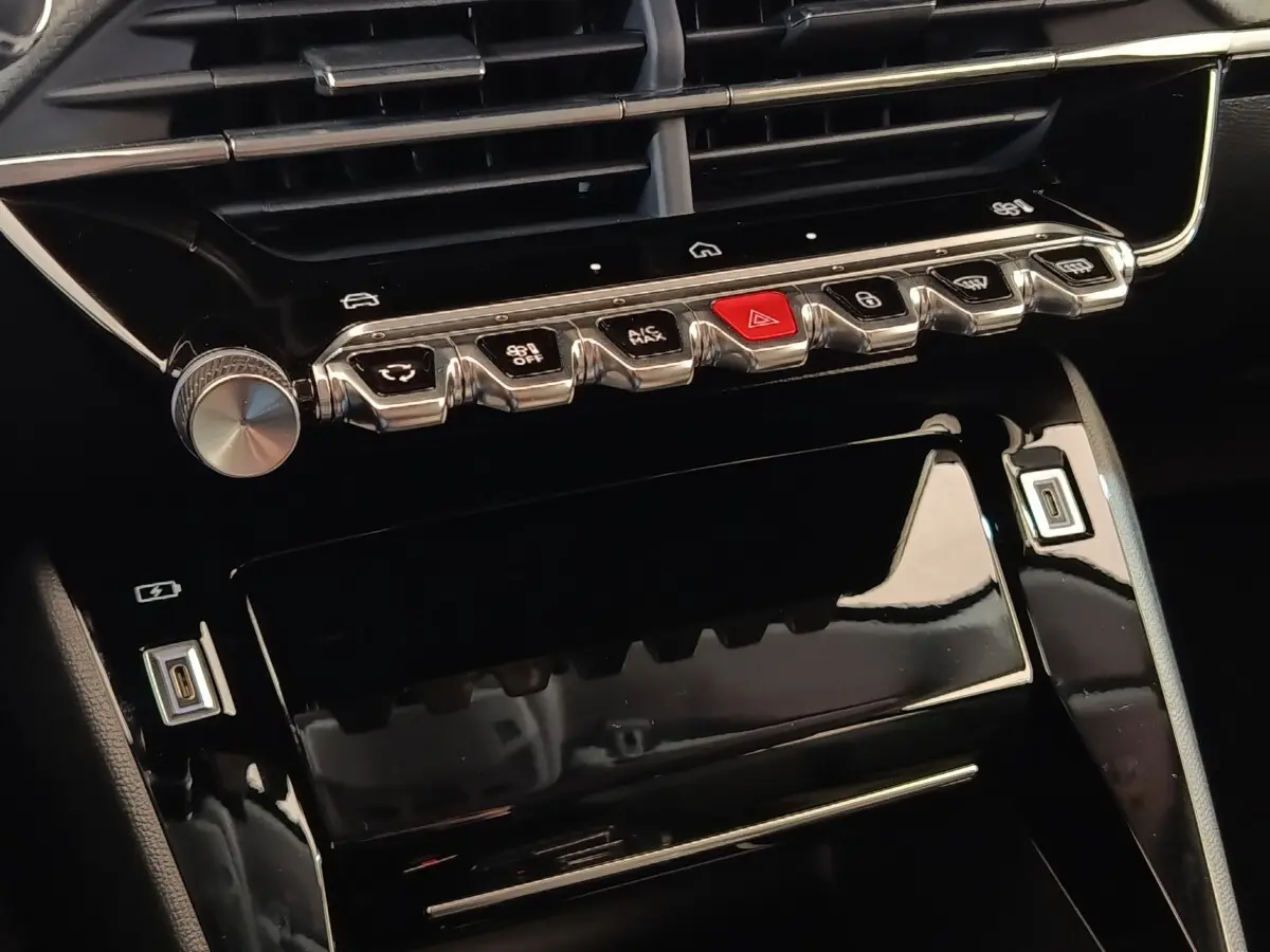 Gros plan sur la console centrale noire brillante du Peugeot 208 électrique 2024 avec commandes tactiles et boutons métalliques.