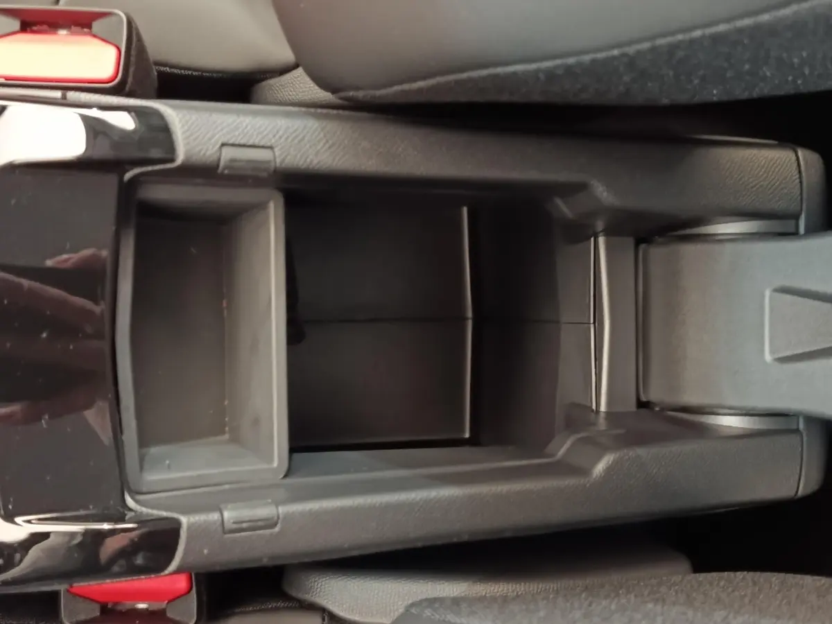 Vue plongeante sur le rangement central noir de la Peugeot 208 électrique 2024, avec accoudoir et bouton de frein à main.