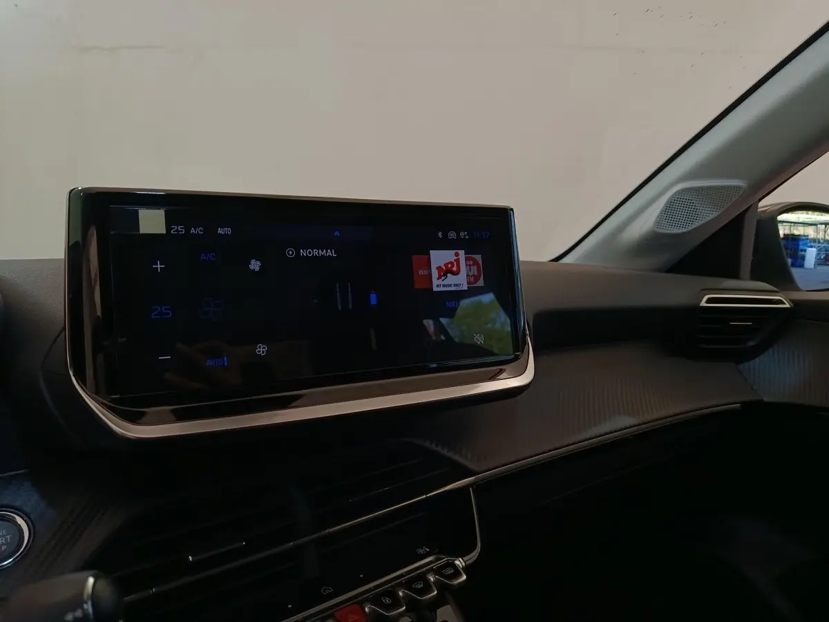 Vue intérieure du tableau de bord de la Peugeot 208 électrique 2024, avec écran tactile central et commandes climatisation digitales.