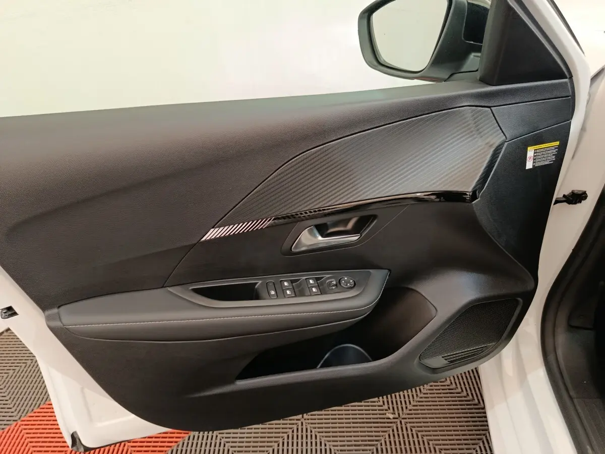 Intérieur côté conducteur de la porte avant droite blanche du Peugeot 208 électrique 2024 avec commandes de vitres et miroir.