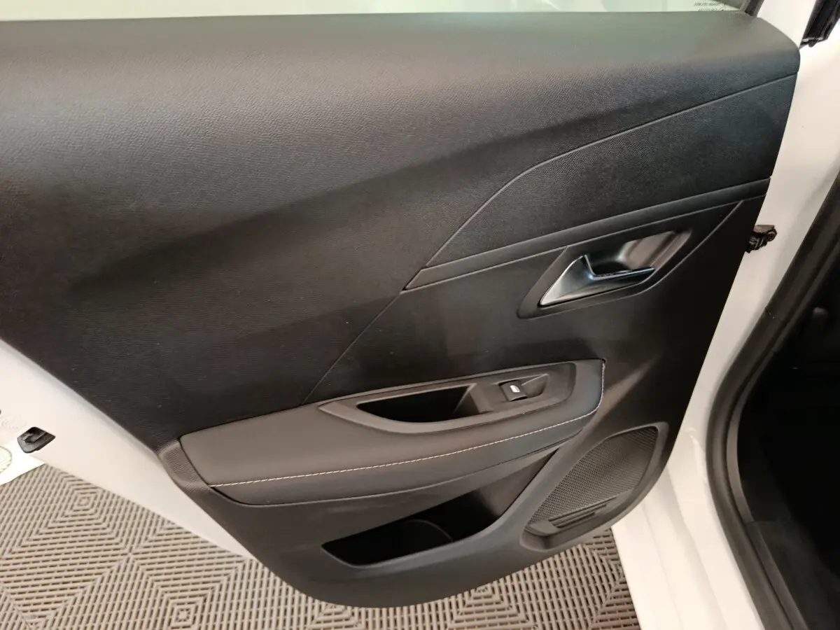 Gros plan sur la porte avant droite noire avec poignée argentée et commande de lève-vitre d’une Peugeot 208 blanche électrique 2024.