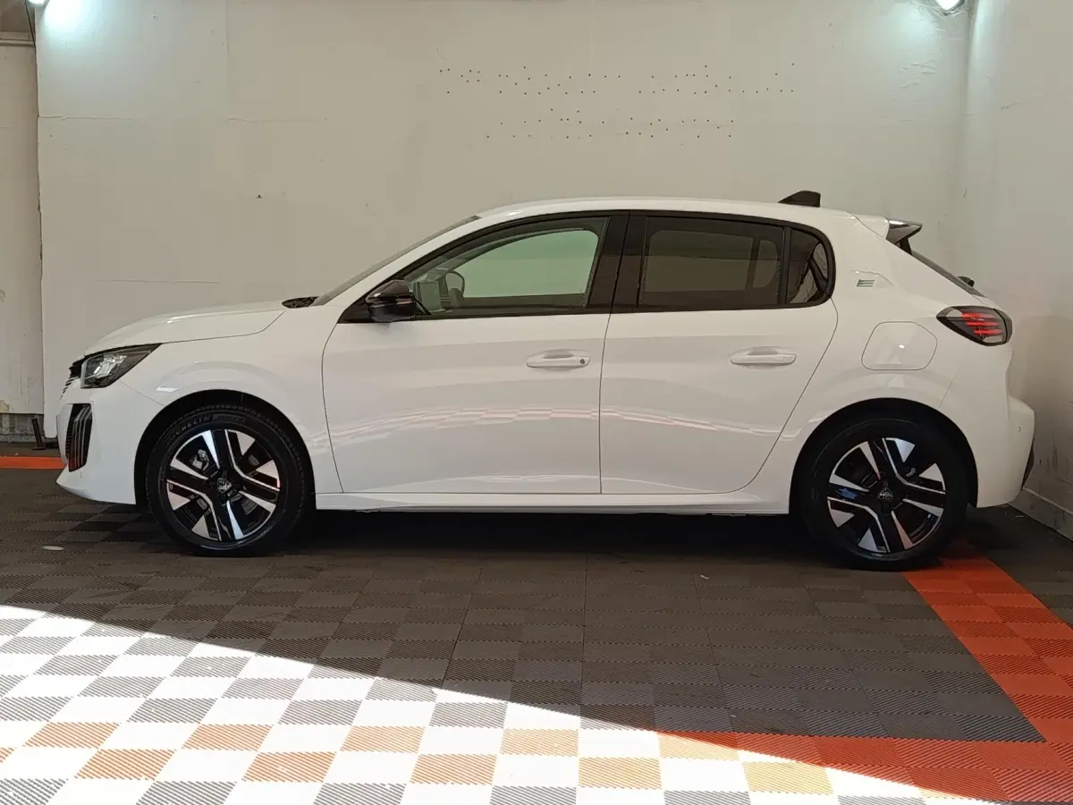 Profil côté droit d'une Peugeot 208 électrique blanche 2024, avec jantes noires et détails modernes sur les feux arrière.