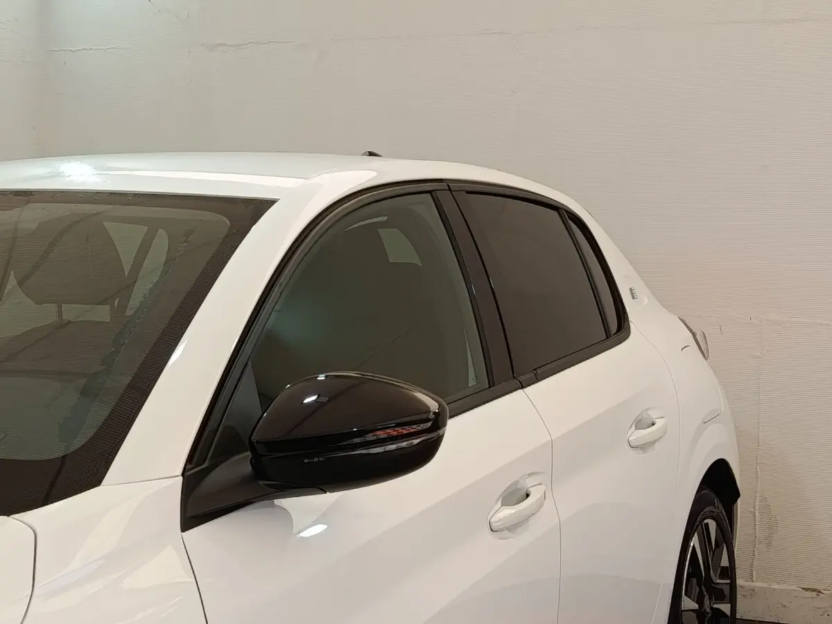 Vue 3/4 arrière gauche d'une Peugeot 208 électrique blanche avec rétroviseur noir et vitres teintées.