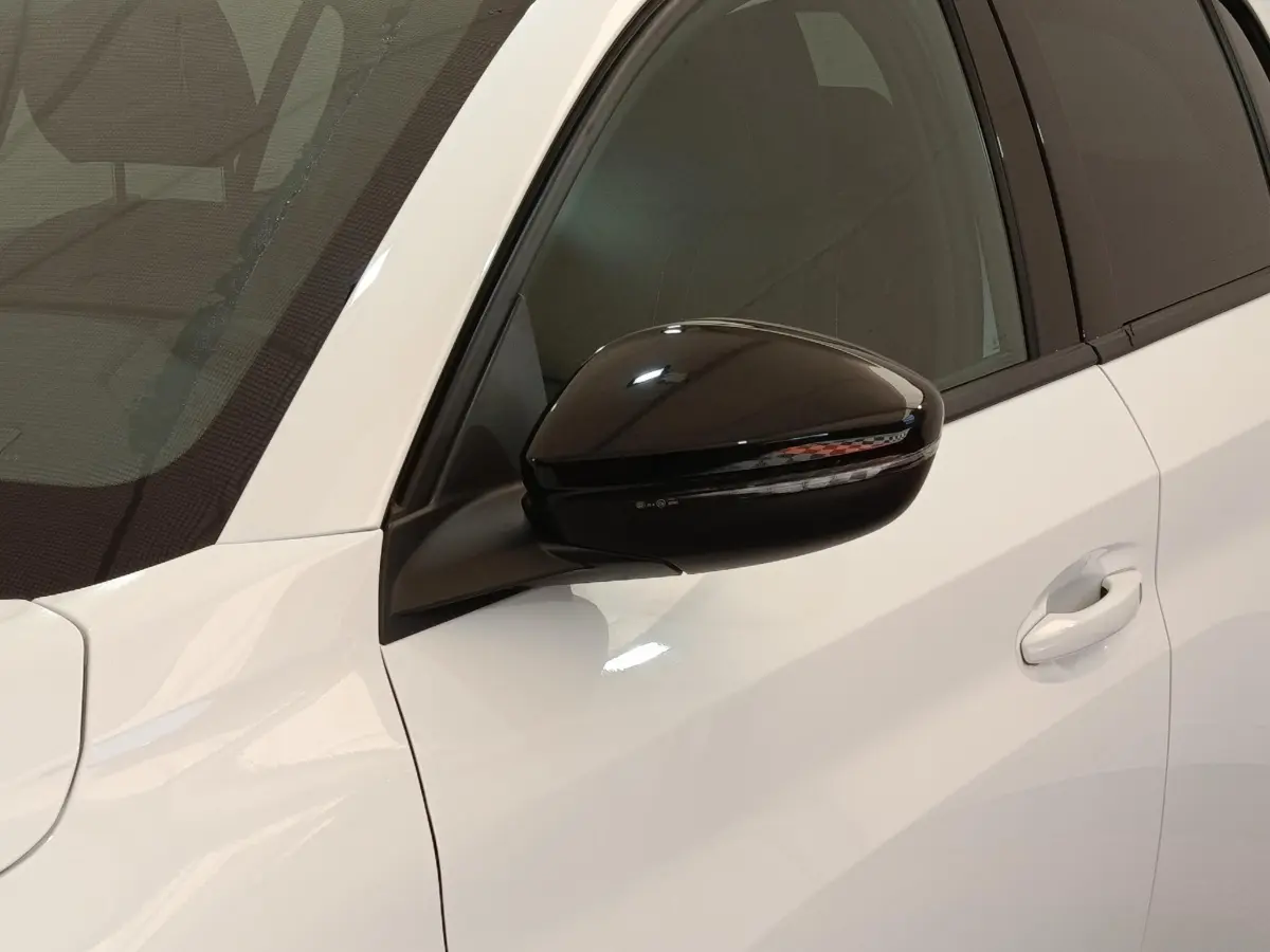 Gros plan sur le rétroviseur noir et la portière blanche côté gauche d'une Peugeot 208 électrique 2024.