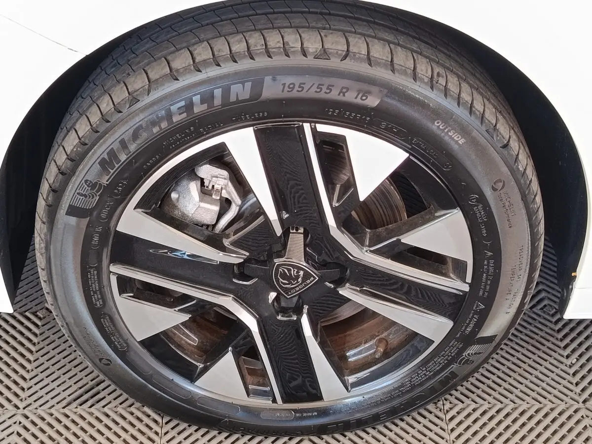 Gros plan sur la roue avant droite blanche d’une Peugeot 208 électrique 2024 avec jante noire et argentée design.