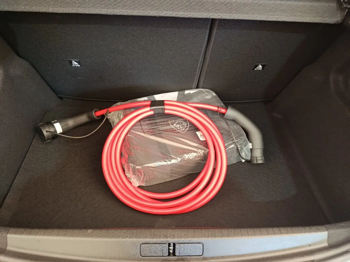 Coffre ouvert d'une Peugeot 208 électrique 2024, montrant un câble de charge rouge enroulé sur fond noir.