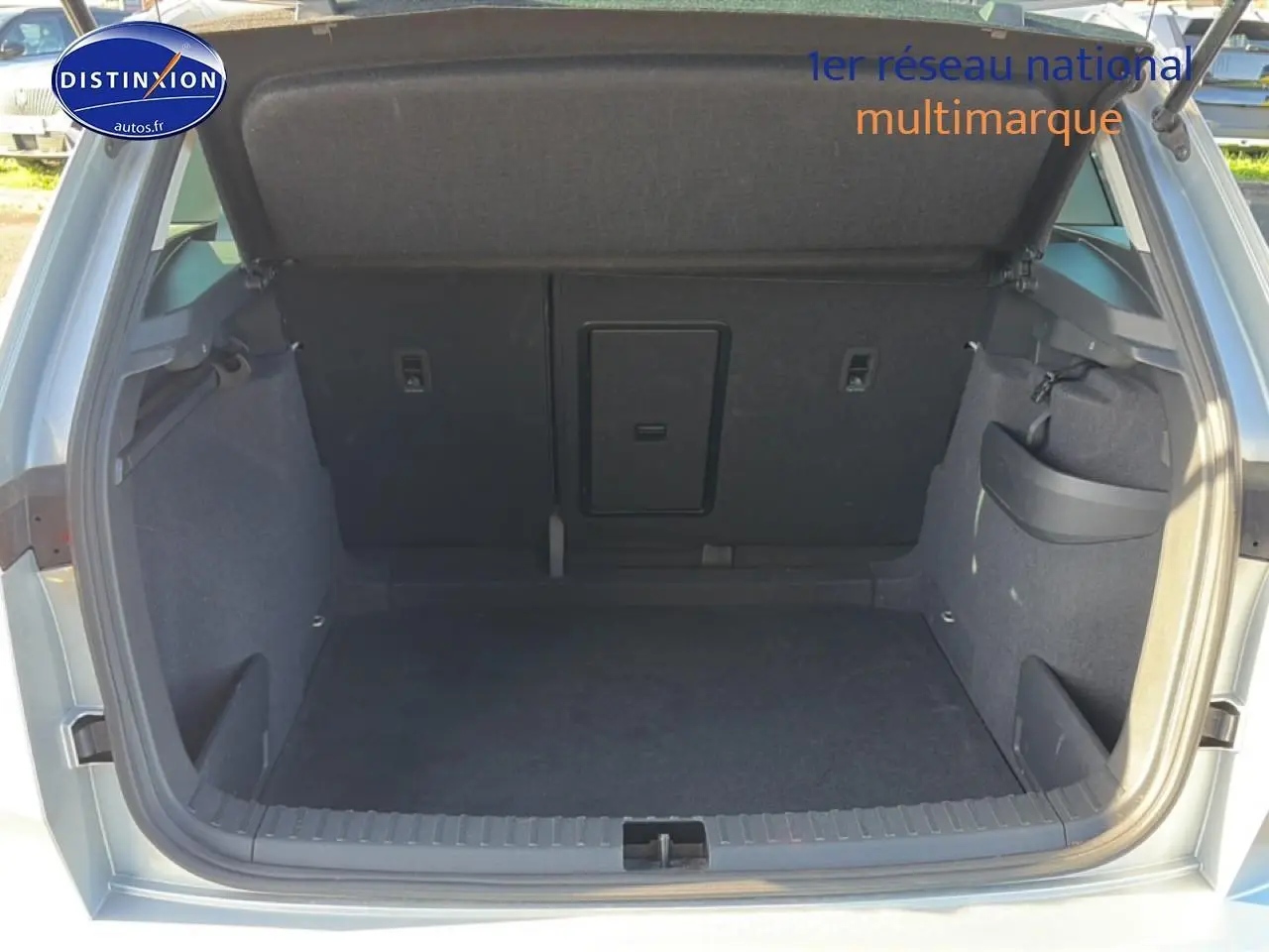 Coffre ouvert vu de l'arrière d'un Skoda Karoq gris, montrant l'espace de chargement et la trappe à skis centrale.