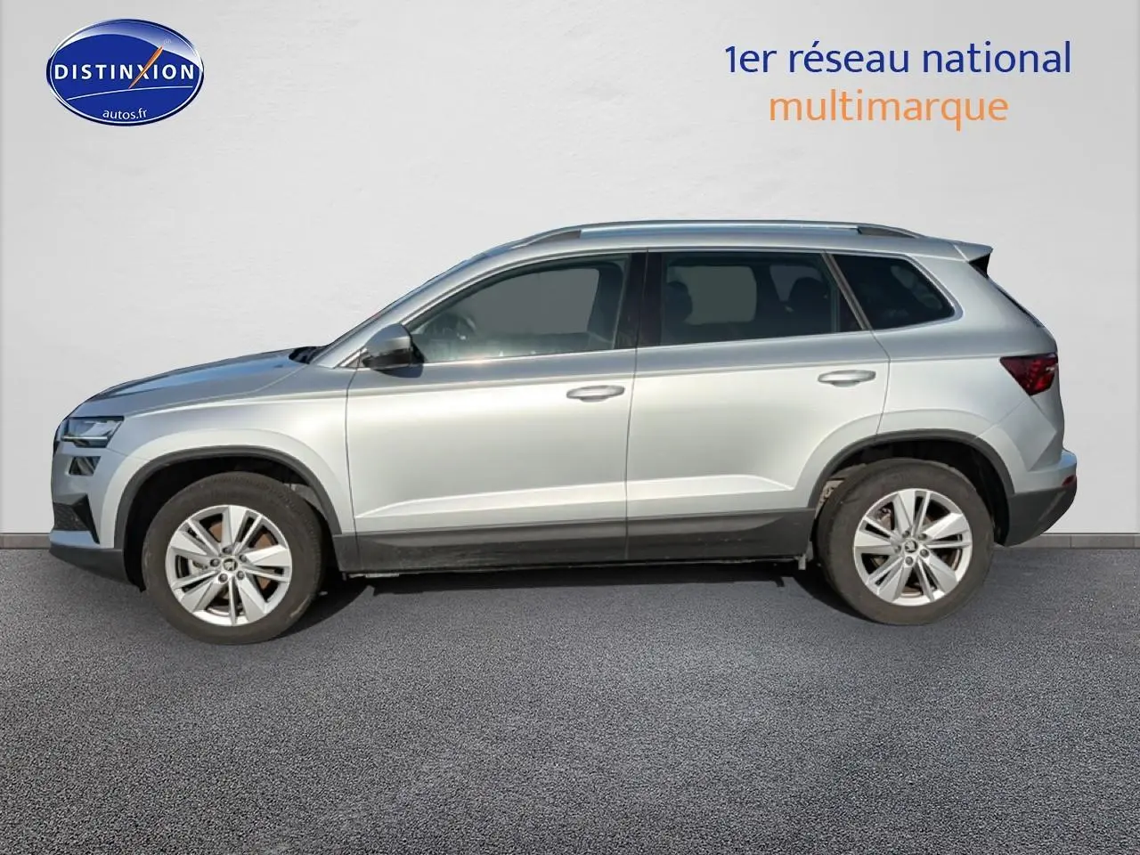 Profil côté gauche d'un Skoda Karoq gris 2025 avec jantes alu et barres de toit visibles.