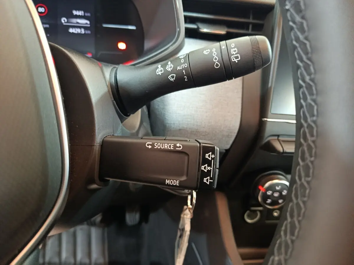 Gros plan sur les commandes au volant d'une Renault Clio noire, avec affichage numérique et volant cuir synthétique visible.