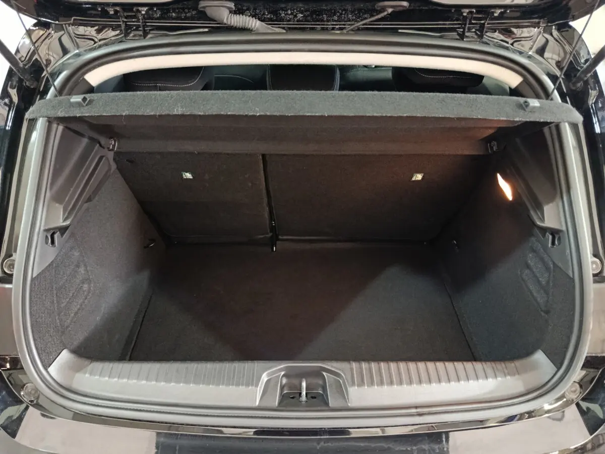 Vue arrière du coffre ouvert d’une Renault Clio noire, montrant l’espace de rangement intérieur et la tablette de séparation.