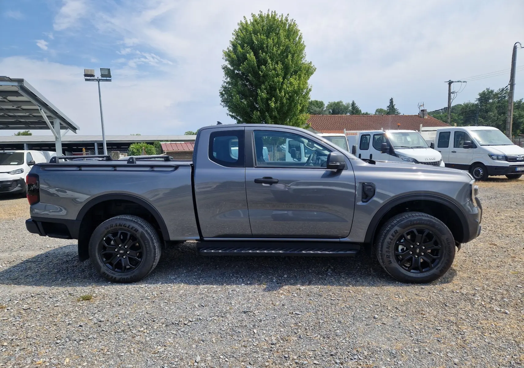 Ford Ranger Super Cabine gris carbone vu de profil côté gauche, avec marchepied et plateau couvert par un rideau rigide.