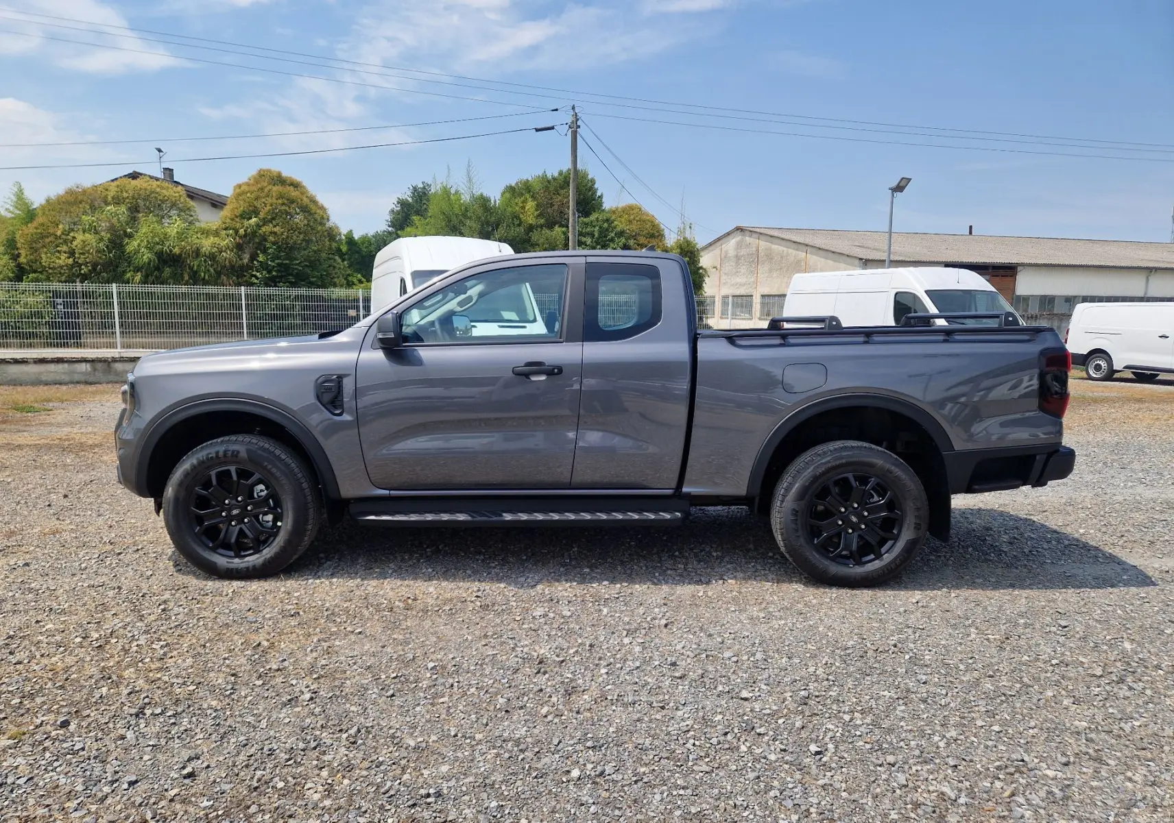Ford Ranger Super Cabine gris carbone vu de profil côté gauche, avec marchepied et barres sur le plateau.